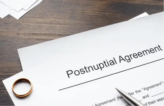 Postnuptial agreement document with a wedding ring and pen on a wooden desk.