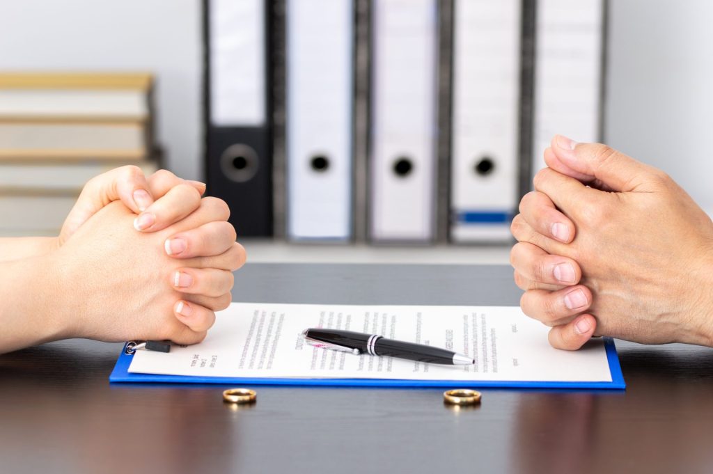 Couple sitting across from each other with divorce papers and wedding rings on a table during a legal separation discussion.