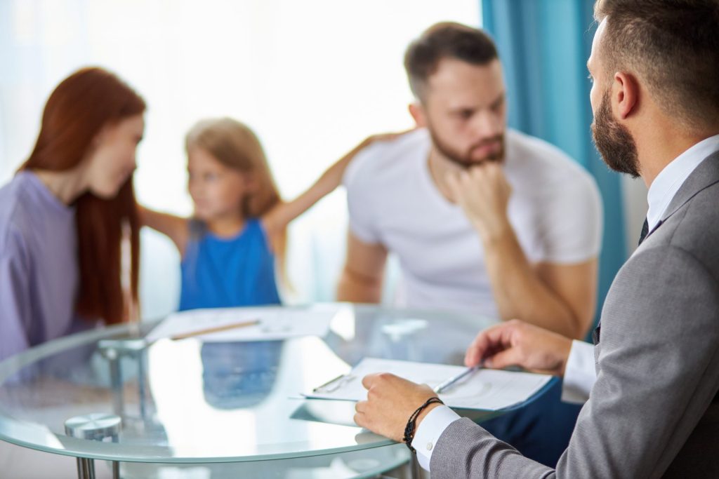 Divorcing parents meeting with a family lawyer while their child sits between them during a custody consultation.